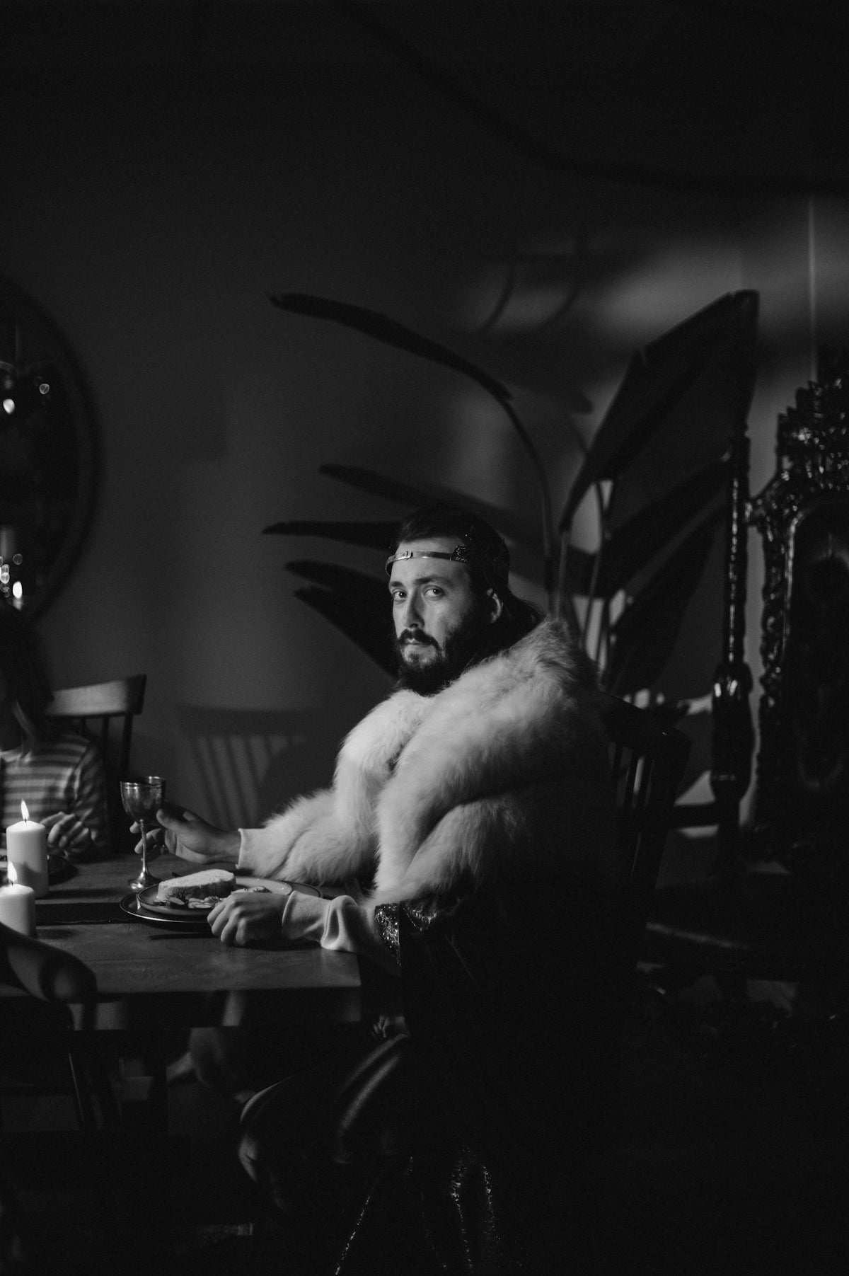Man in fur coat holding wine glass at table.