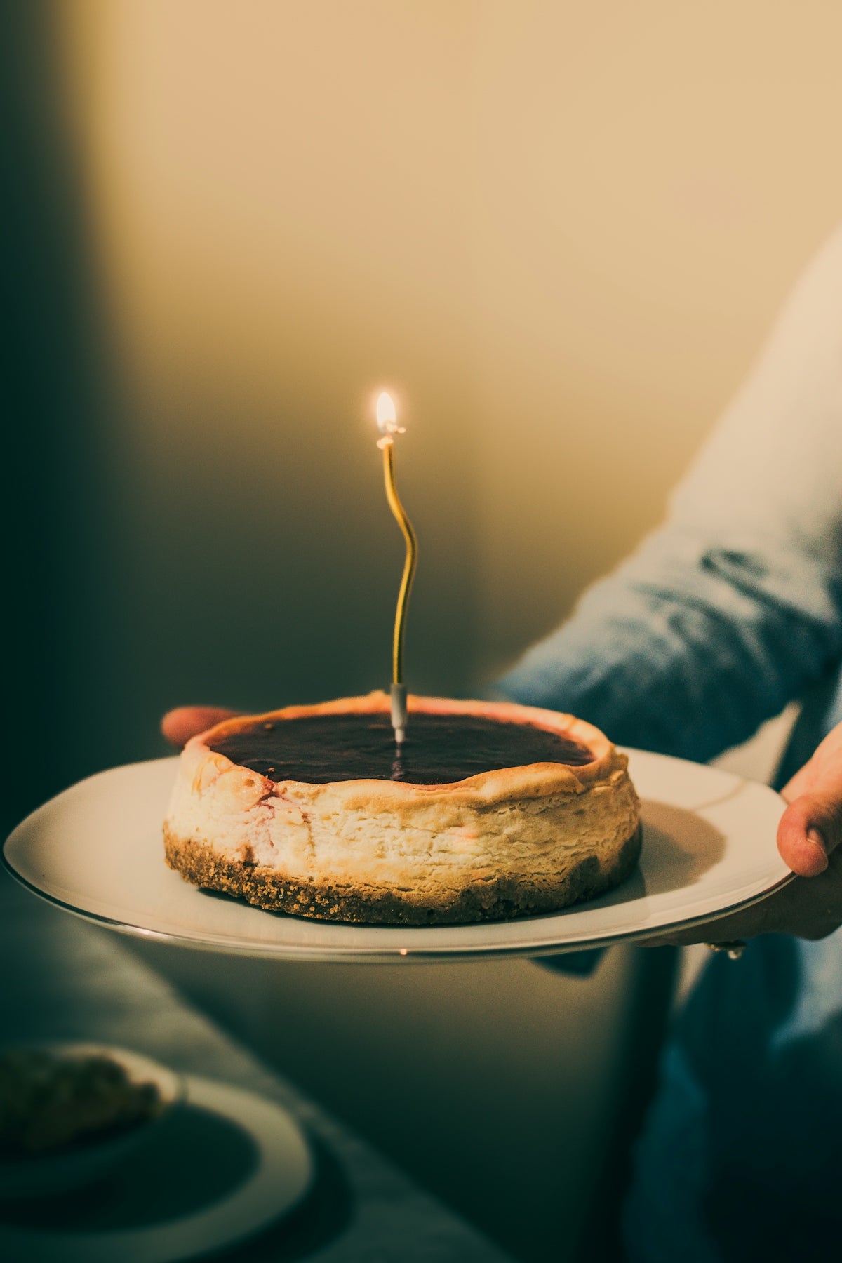 A cheesecake with a single lit candle on a plate