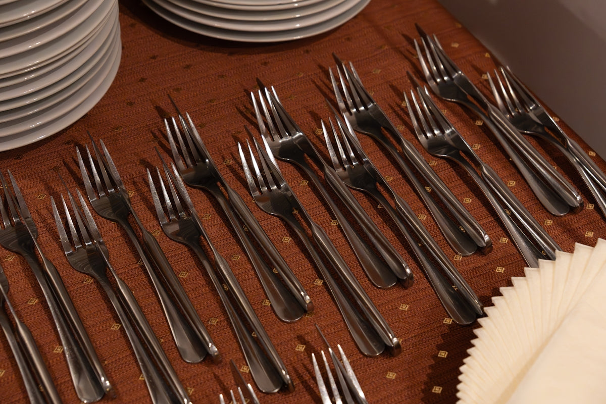 Many silver forks arranged on a wooden table with plates.
