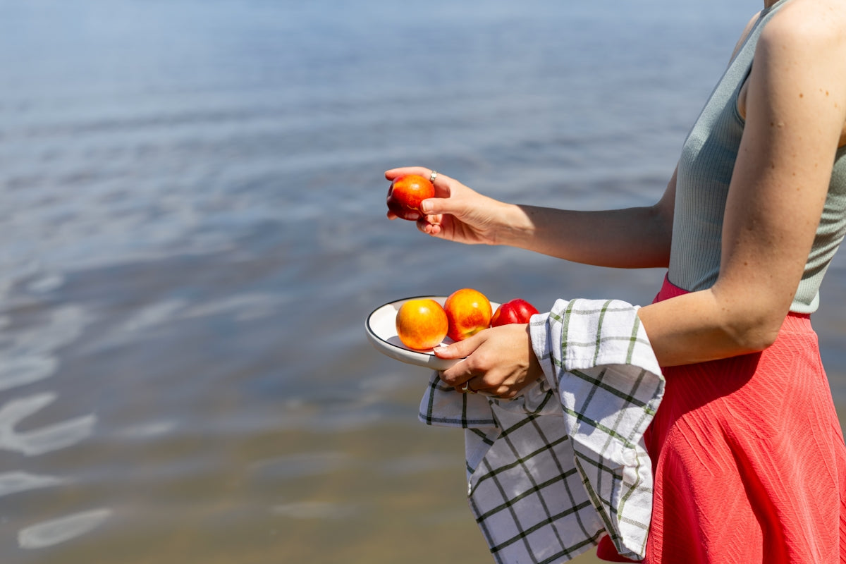 Woman holding a plate of fresh fruit by the water.