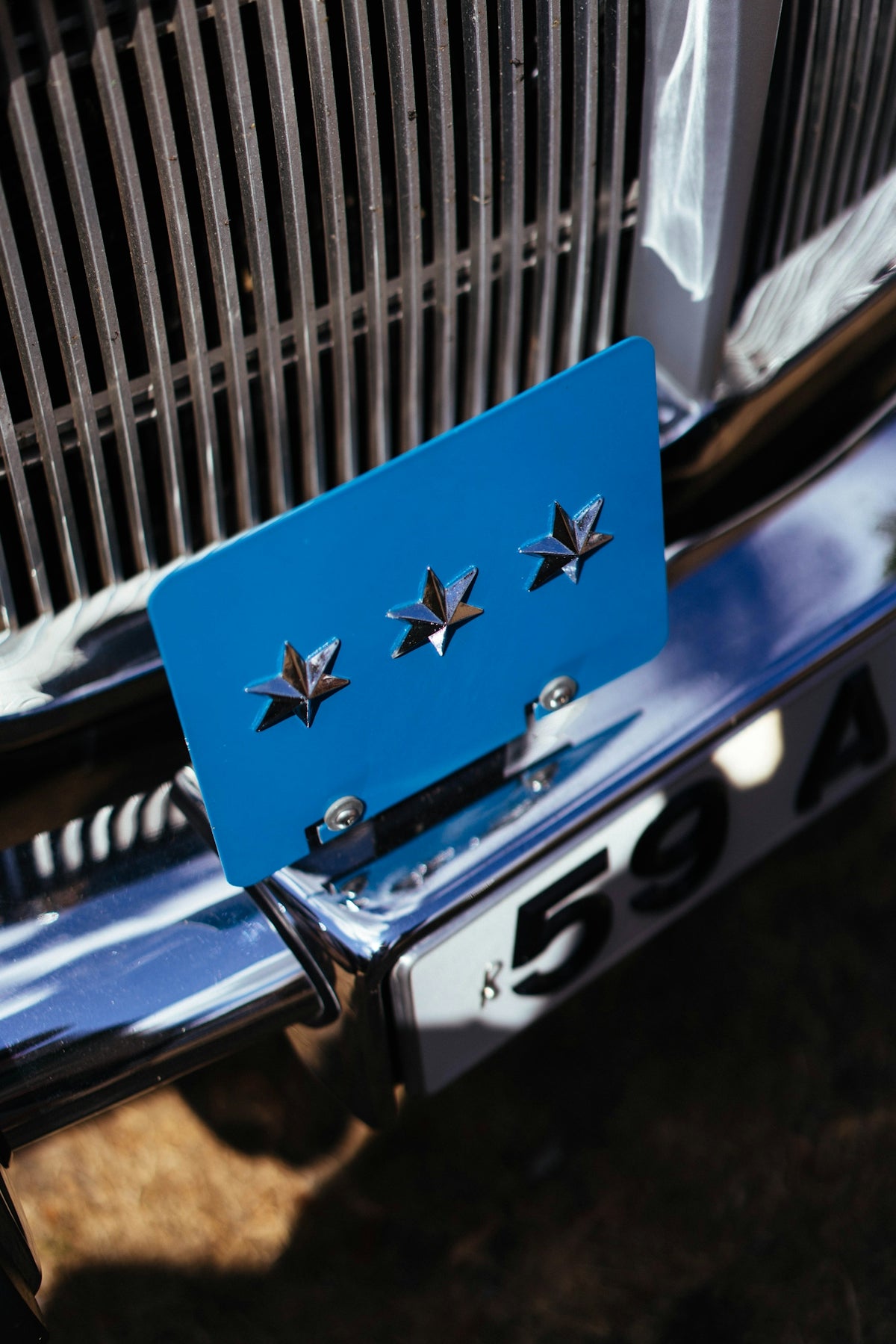 Vintage car front featuring a blue plate with three stars.