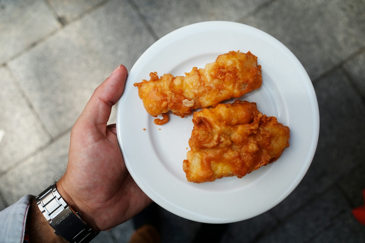 A hand holding a white plate with two pieces of golden fried fish
